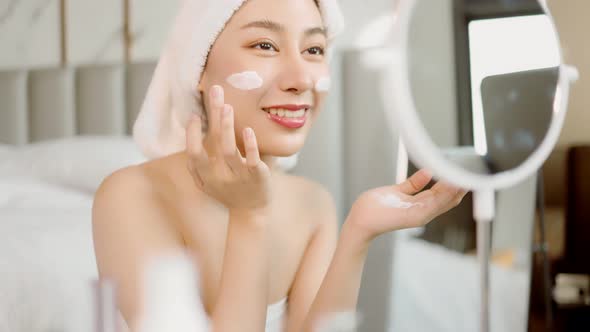 Happy attractive asian woman apply skincare cream on face and body.