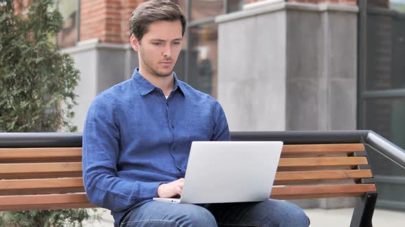 Young Man working on Laptop, Sitting Outdoor on Bench