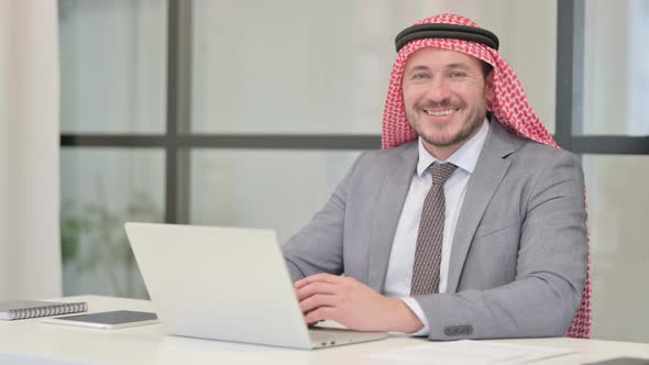 Middle Aged Arab Businessman Smiling at Camera while using Laptop in Office