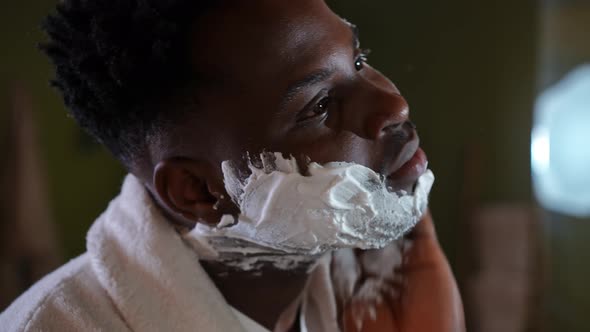 Closeup Side View Face of Concentrated African American Young Man Applying Shave Foam on Skin