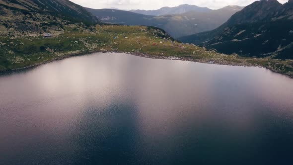 Wide aerial drone slowly flying over a lake looking down onto a valley a mountain range.