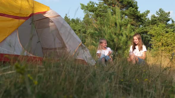 Two girls are sitting near the tent and talking.