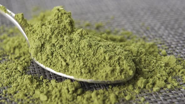 Organic green matcha tea powder in a teaspoon on a gray mat