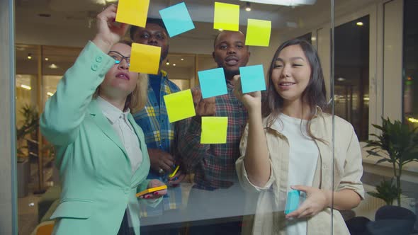 Business Team Write Ideas on Sticky Notes on Glass