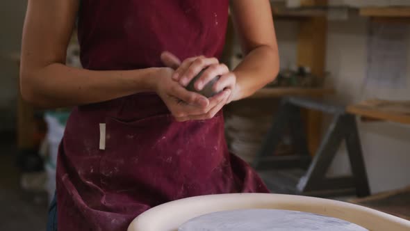 Mid section of female potter keeping a ball of clay on potters wheel at pottery studio