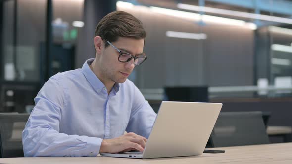 Young Man with Laptop Thinking at Work