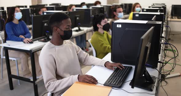 Young multiracial students using computers inside class room while wearing safety masks