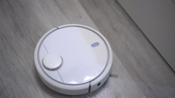 A White Robot Vacuum Cleaner Rides on a White Parquet Floor