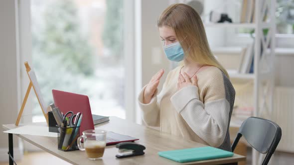 Focused Slim Young Woman in Covid19 Face Mask Using Sign Language Talking in Video Chat at Home