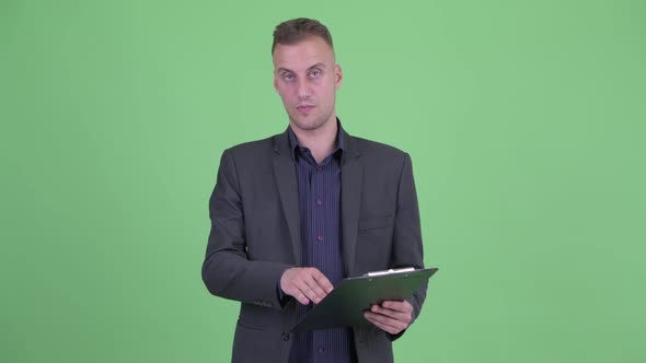 Happy Handsome Businessman in Suit Talking While Holding Clipboard