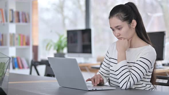 Pensive Young Asian Woman Using Laptop in Office 