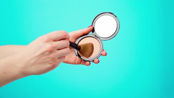 Female Hands Holding Face Powder Makeup Product and Face Brush Against Blue Background