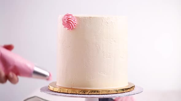 Baker piping pastel color buttercream rosettes on a white cake to make a unicorn cake.