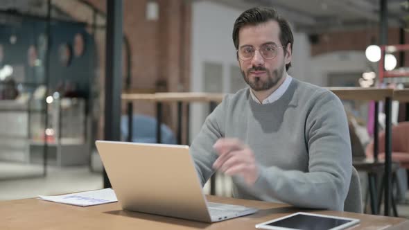 Young Man Pointing at Camera While Using Laptop in Office