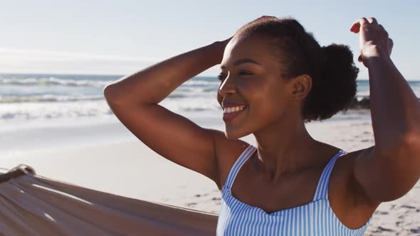 Close up of african american woman smiling while sitting on a hammock at the beach