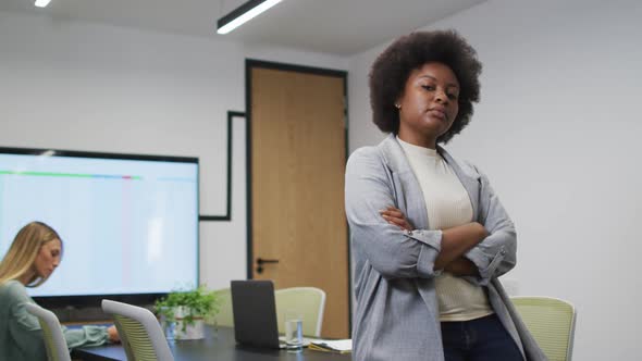 Portrait of african american businesswoman smiling in office, with colleague working in background