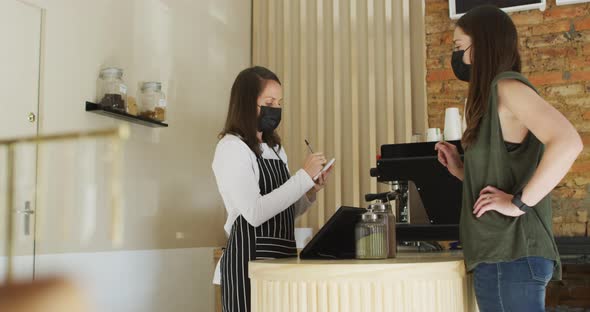 Caucasian waitress wearing face mask taking order from caucasian female customer