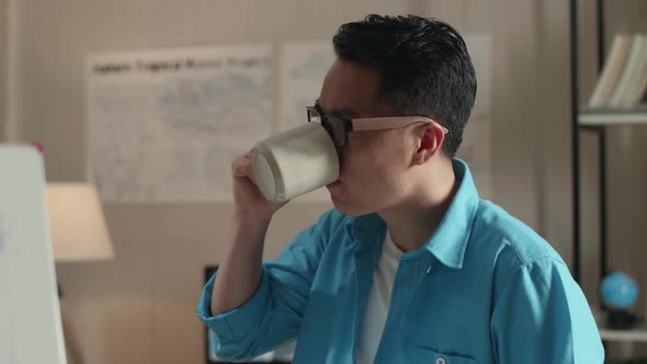 Close Up Of Asian Man Engineer Sitting On The Table And Drinking Coffee While Using A Laptop To Work