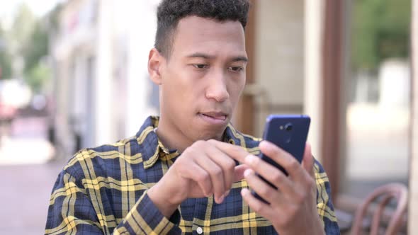 African Man Celebrating Online Success on Smartphone, Outdoor