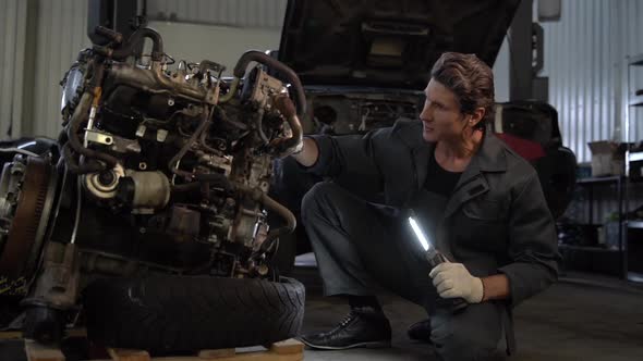 Waist up portrait image of senior serious mechanic in uniform standing near the detail of the car