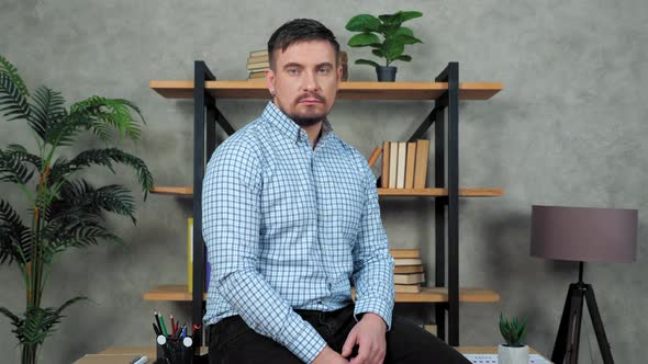 Serious man business coach sitting at desk in office turns head looking camera