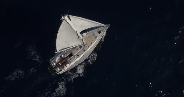 Top Down to 70 - 80 degree tilted slow tracking shot of monohull sail boat moving around while saili
