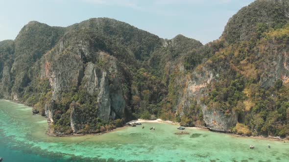 Tall Limestone cliffs adjacent to shallow emerald green shoreline in Tonsai Bay, Ko Phi Phi Island