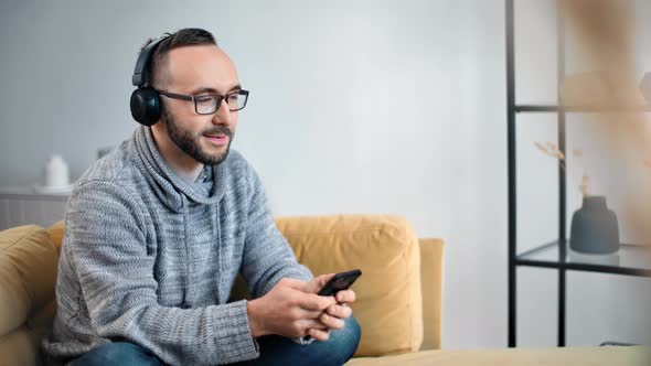 Relaxed Guy Wearing Headphones Enjoying Audio Sound on Yellow Couch