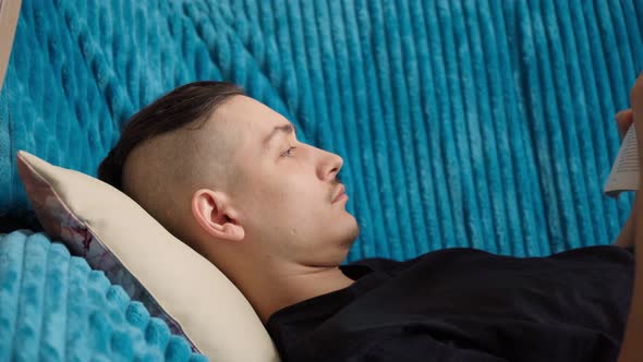 Handsome Man in Casual Wear Lying on Sofa Reading Book