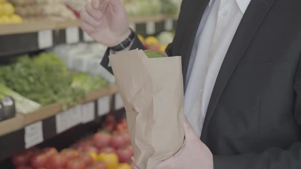 Unknown Caucasian Man in Suit Putting Pomelo Into Paper Shopping Pack and Leaving. Unrecognizable