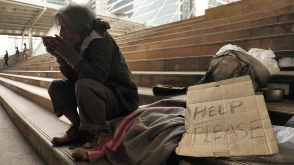 Homeless old man eating soup received from volunteers while sitting on stairs in the city