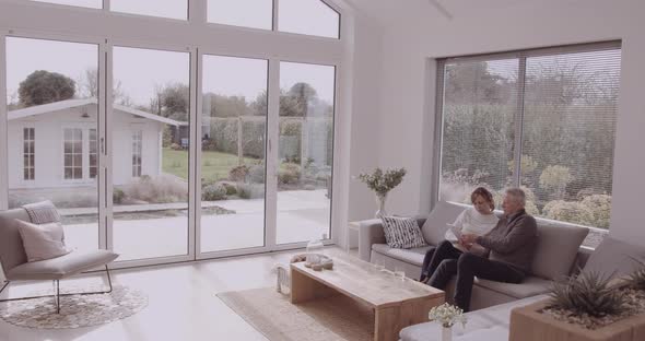 Senior adult couple at home on sofa looking at digital tablet