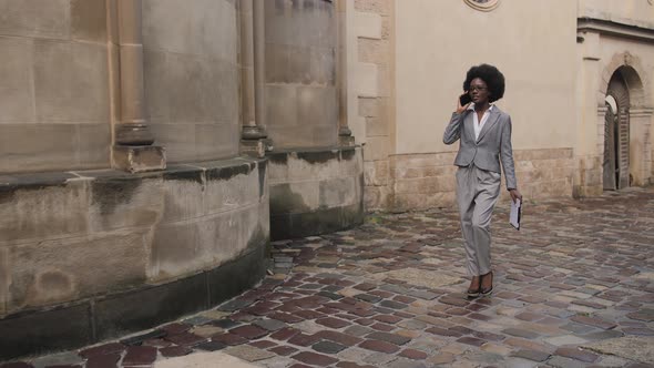 Stylish Business Lady in Eyeglasses Having Mobile Conversation While Walking on City Street