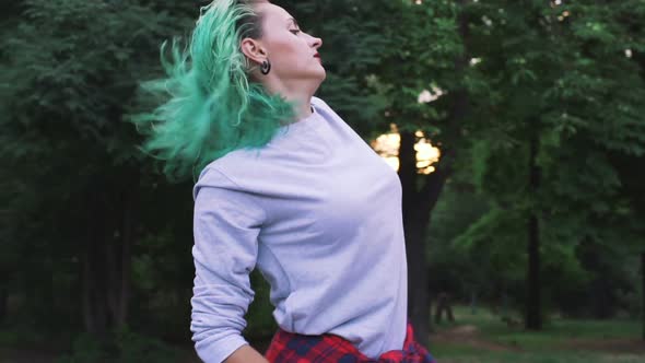 Young Stylish Funky Girl with Green Hair Riding Roller Skates and Dancing in Park Slow Motion