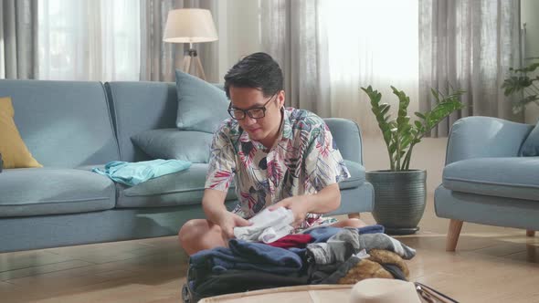 Asian Young Man Packing Clothes In Suitcase At Home, Preparing For Vacation