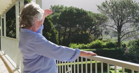 Smiling caucasian senior woman at home enjoying view of sunny garden from balcony