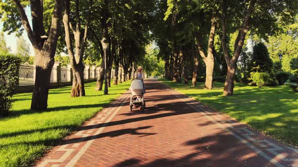 Front View of Young Mother with Pram in the Sunny Park