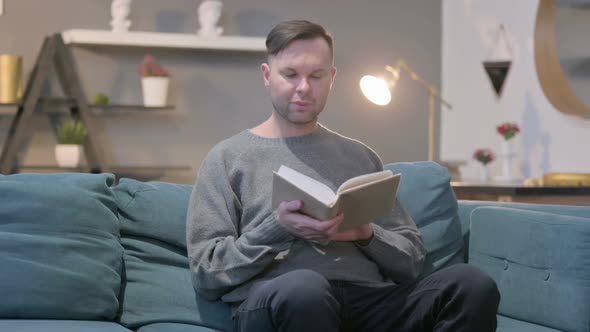 Casual Man Reading Book While Sitting in Sofa