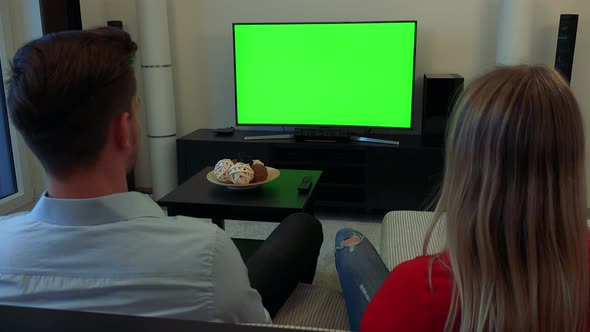 A Man and a Woman (The Backs of Their Heads) Watch a TV with a Green Screen in a Cozy Living Room
