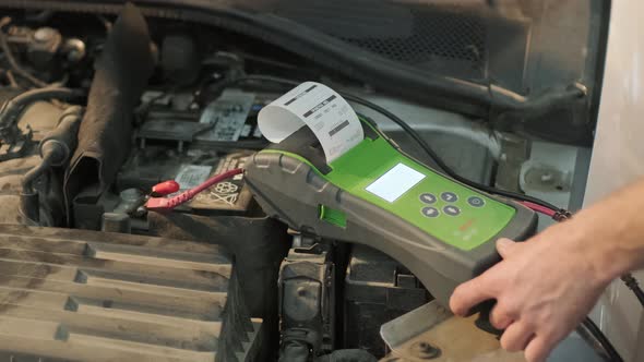 Auto service worker checking voltage on car battery. Service engineer working in car service station