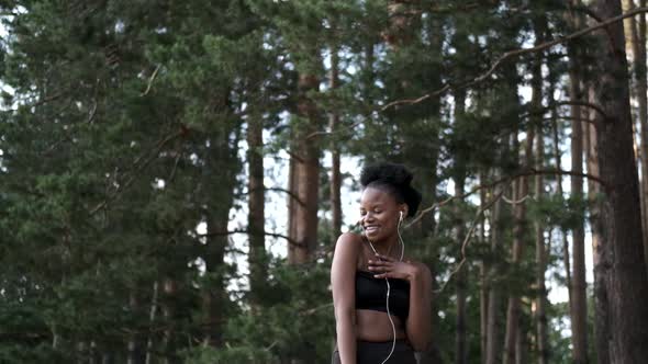 Young African Girl with Curly Hair in Headphones Dancing and Having Fun on a Background of Nature. A