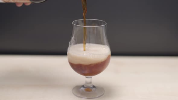 Close up view of man pouring dark beer into glass isolated on dark background.