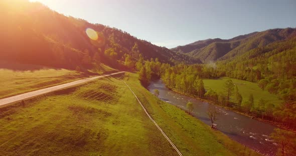 Mid Air Flight Over Fresh Mountain River and Meadow at Sunny Summer Morning. Rural Dirt Road Below.