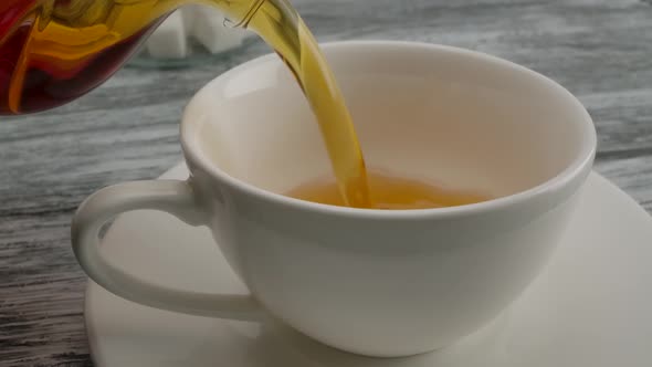 Pouring Black Tea Into a Classic White Cup on a Saucer From Teapot