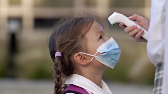 Little Schoolgirl in a Protective Mask is Checked the Temperature