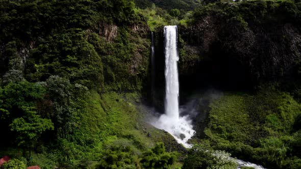 Aerial view, zooming in a a large waterfall until close to the water falling down and splashing