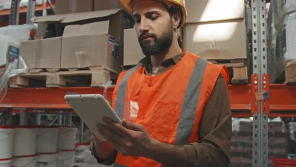 Worker in Hard Hat Using Tablet in Warehouse
