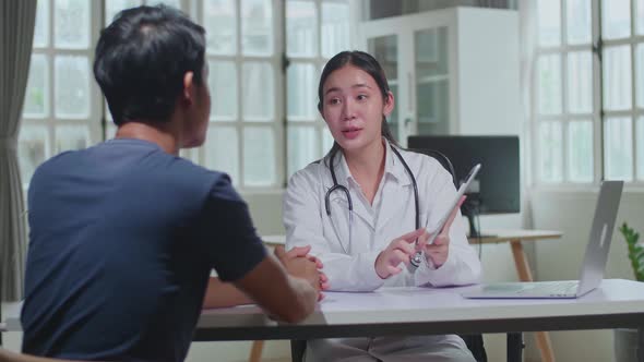 Asian Female Doctor Showing Analysis Results On Tablet Computer To Male Patient During Consultation
