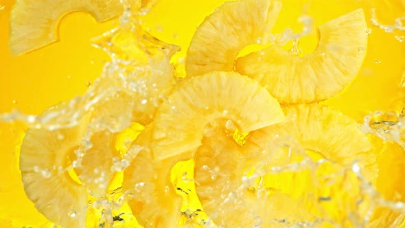 Super Slow Motion Shot of Pineapple Slices Falling Into Water on Yellow Background at 1000Fps