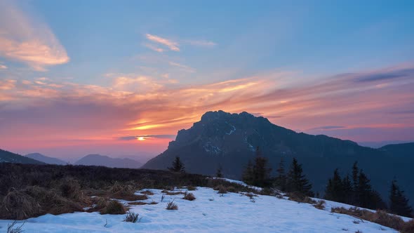 Beautiful nature sunset over high rocky mountain, snow with structures on the meadow, early spring